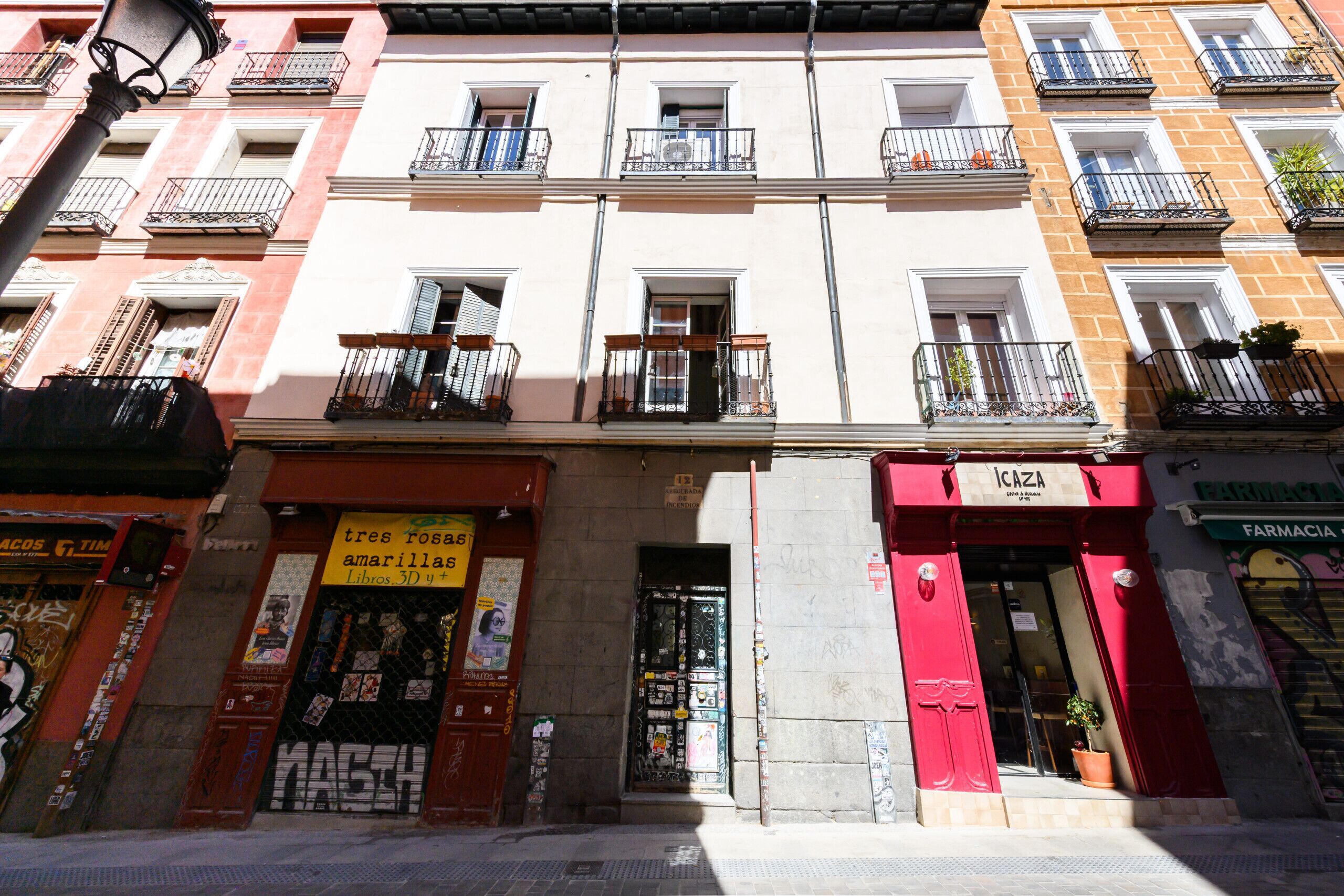 Un edificio de varios pisos con balcones, una farmacia y una tienda con toldo rojo.