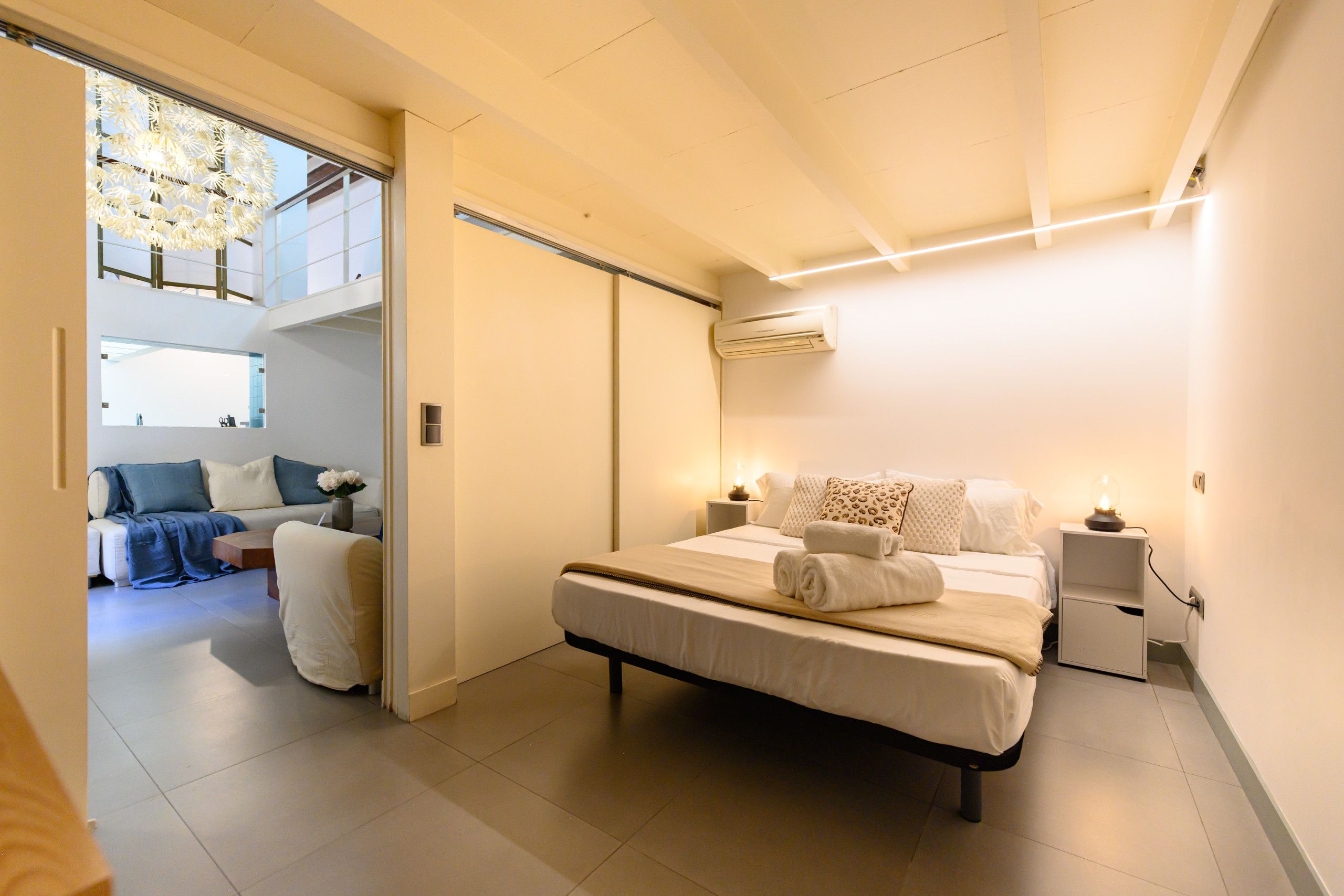 Een moderne slaapkamer met een bed, nachtkastjes en uitzicht op een zithoek.