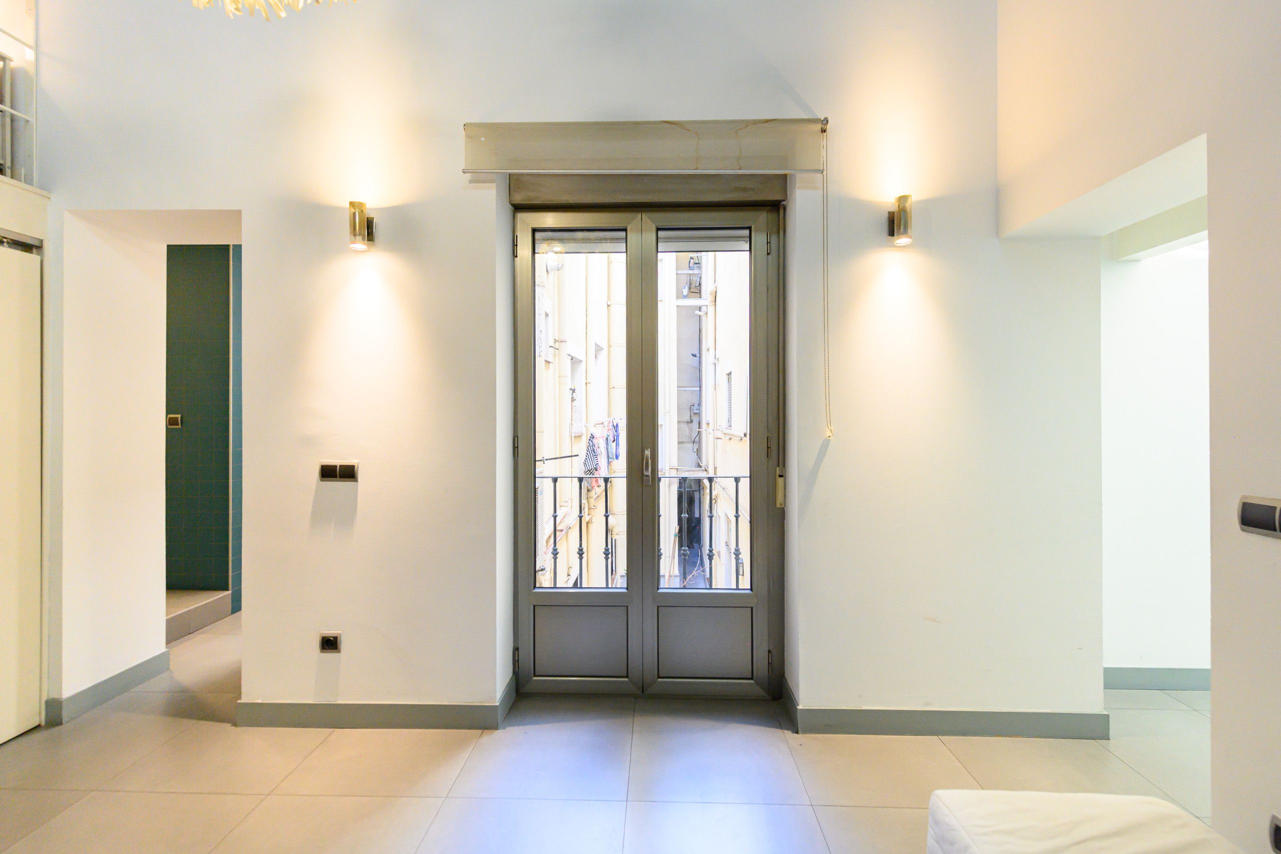 Entrada de hotel con puertas dobles, una lámpara en la pared y piso de baldosas.