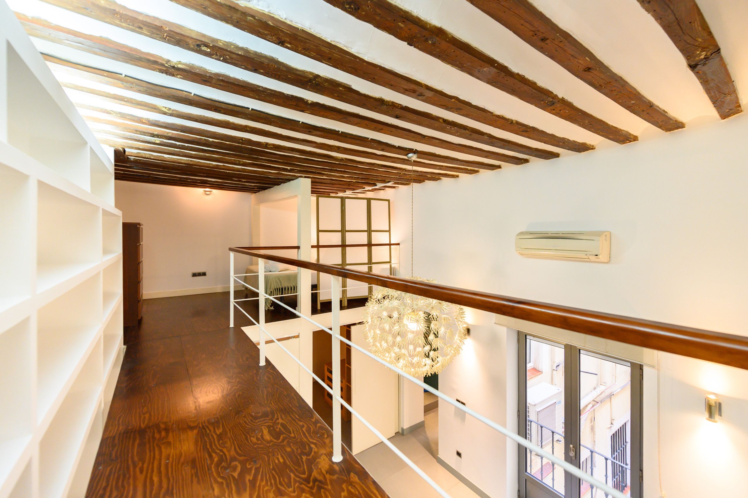 Una escalera de madera con barandilla de vidrio, una pared blanca con radiador y vistas al exterior.
