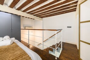 A bedroom with a wooden ceiling, a bed with white linens, a grey wardrobe, and a staircase with a glass railing. - (ESA121ID) Spacious Duplex in the center of Madrid (Madrid)