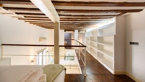 Una camera d'albergo con soffitto in legno, balcone in vetro e un letto bianco.