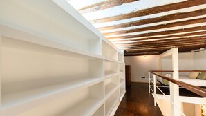 Una camera mansardata con soffitto in legno, scaffali bianchi e un letto a castello.