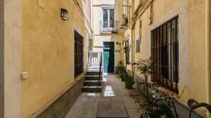 Un stretto vicolo con una scala che conduce all'ingresso di un edificio, piante in vaso e una porta ben visibile.