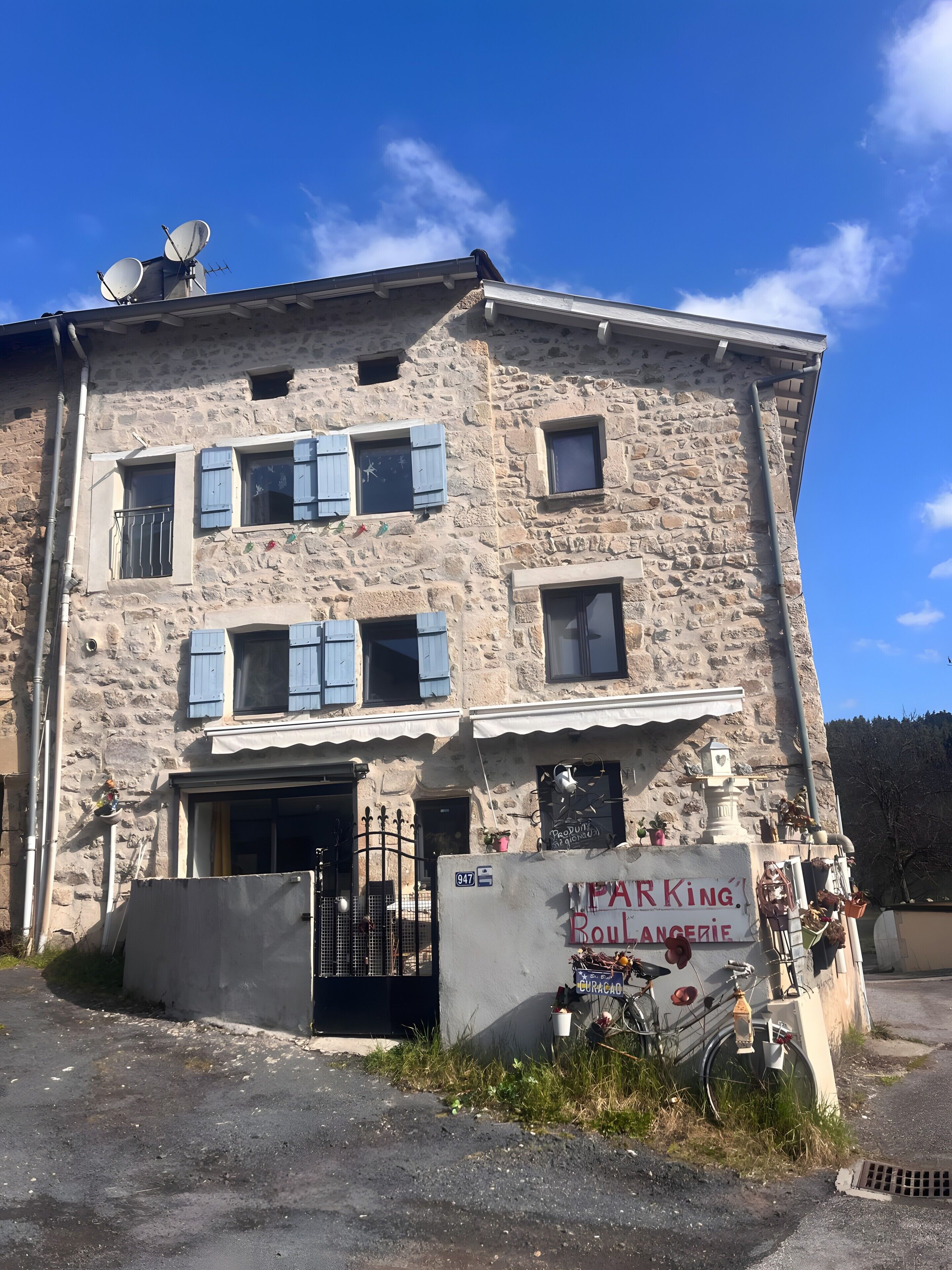 Un bâtiment en pierre doté de nombreuses fenêtres, un panneau indiquant un parking et un vélo garé à l’extérieur.