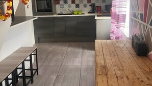 A modern kitchen with a microwave, oven, and sink. There is a wooden table and chairs, and a patterned wall.