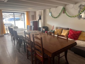Un coin repas avec une table et des chaises en bois, un canapé avec des coussins et une vue sur l’extérieur à travers une porte vitrée.