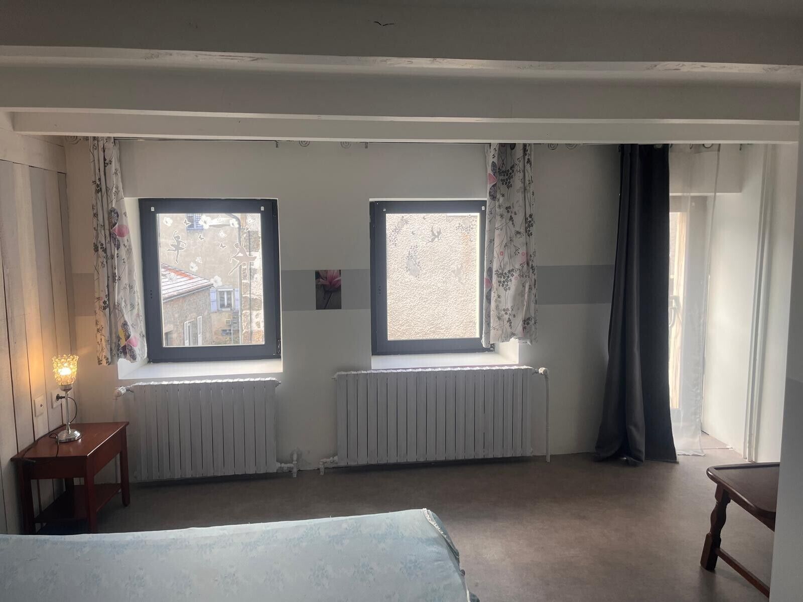 Een slaapkamer met twee ramen, een radiator, nachtkastje en een bed.