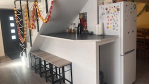 A kitchen with a white refrigerator, a wooden bench, and a staircase with red and yellow decorations.