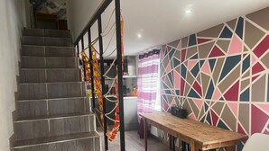 A staircase leading to a kitchen area with a geometric-patterned wall and a wooden table.