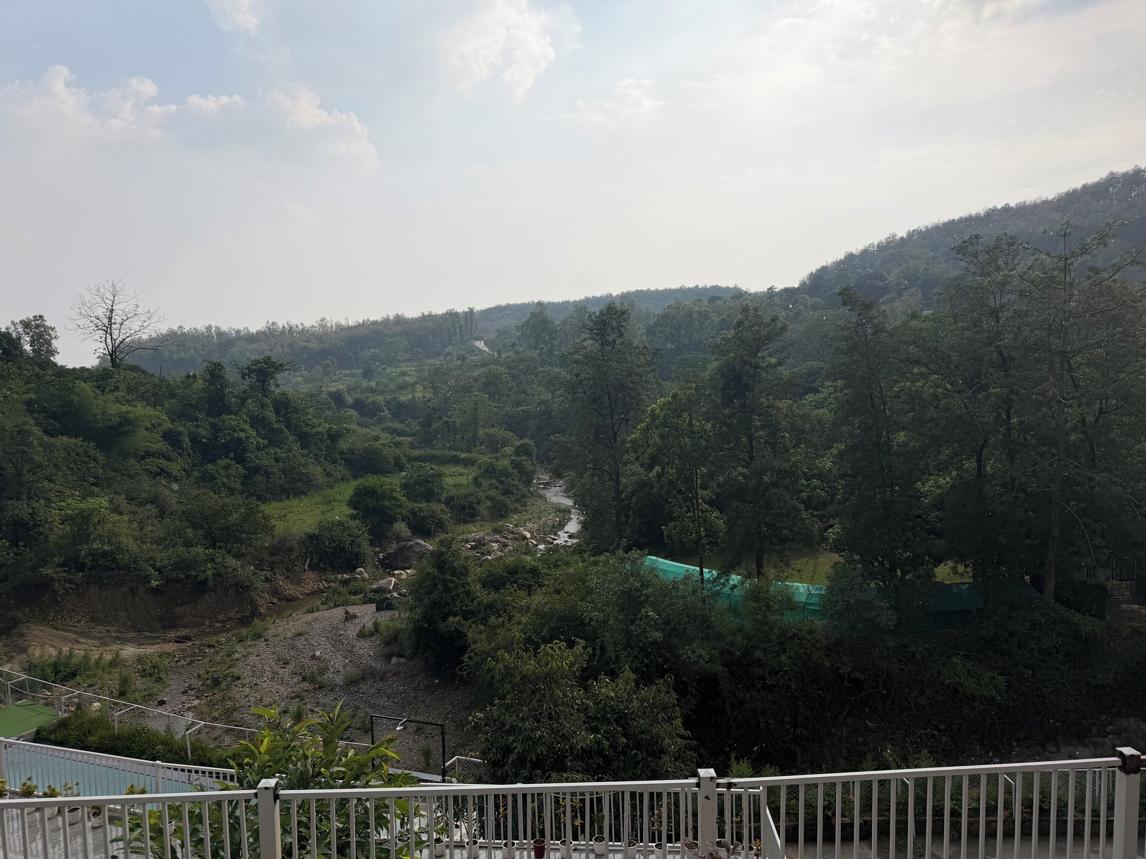 A view of a lush valley with a river, dense greenery, and a distant road.