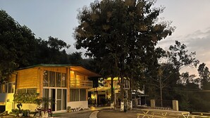 A modern wooden house with a balcony, surrounded by potted plants and a paved walkway. - Saraiville - Boutique Riverside Stay (Vikasnagar)