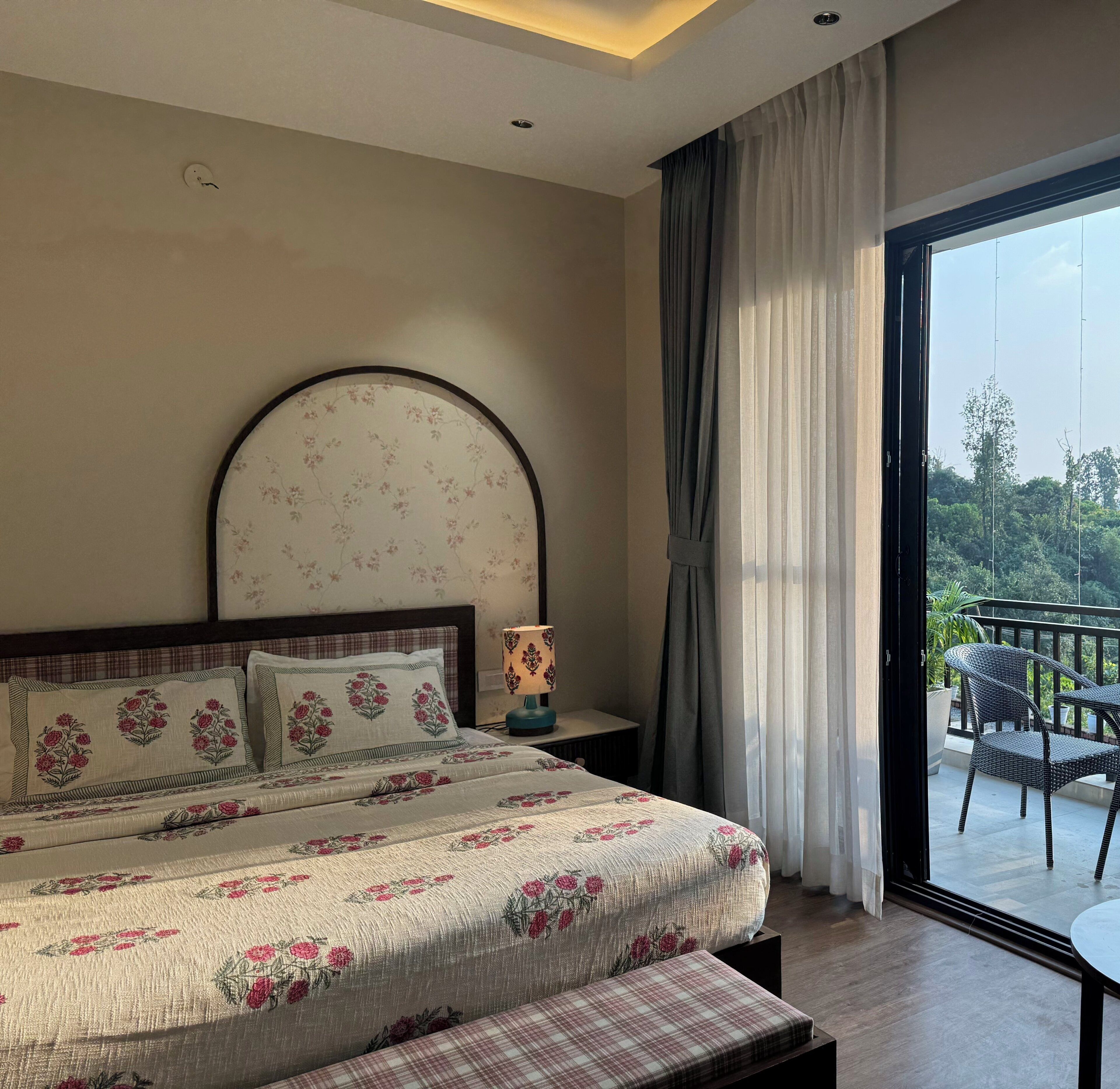 A bedroom with a large bed, a bedside table with a lamp, a view of the outdoors through a balcony door.