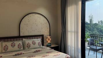A bedroom with a large bed, a bedside table with a lamp, a view of the outdoors through a balcony door.