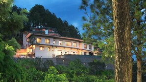 A large, multi-story building with a prominent staircase, surrounded by trees and a stone wall. - Hotel Sonamgang (Punakha)