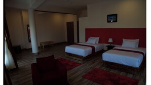 A hotel room with two beds, a red chair, a wooden bench, and a red rug. - Hotel Sonamgang (Punakha)