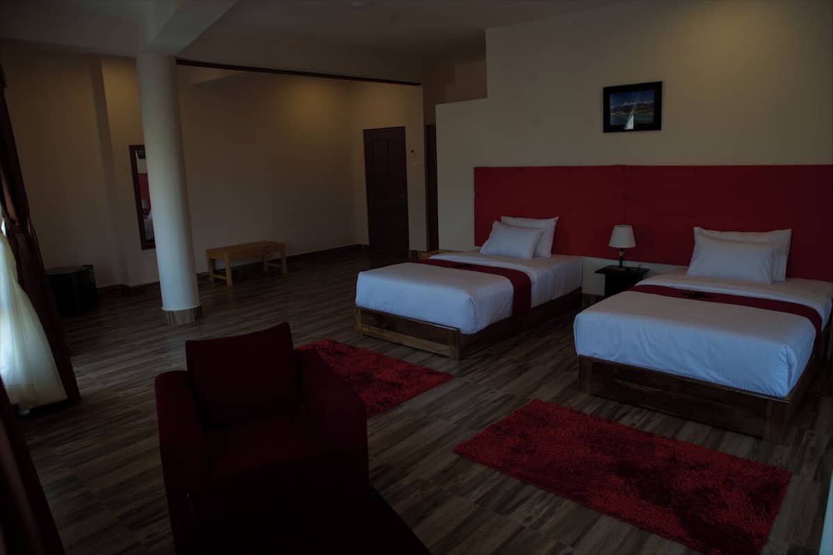 A hotel room with two beds, a red chair, a wooden bench, and a red rug.