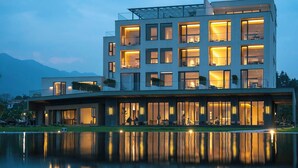Een modern, meerlaags gebouw met grote ramen, een plat dak en een reflecterend waterlichaam ervoor.