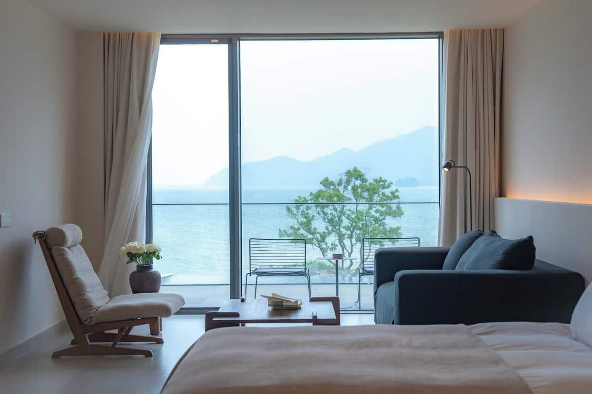 Ein Hotelzimmer mit großem Fenster, einem Bett, einem Sofa, einem Sessel und einem kleinen Tisch.