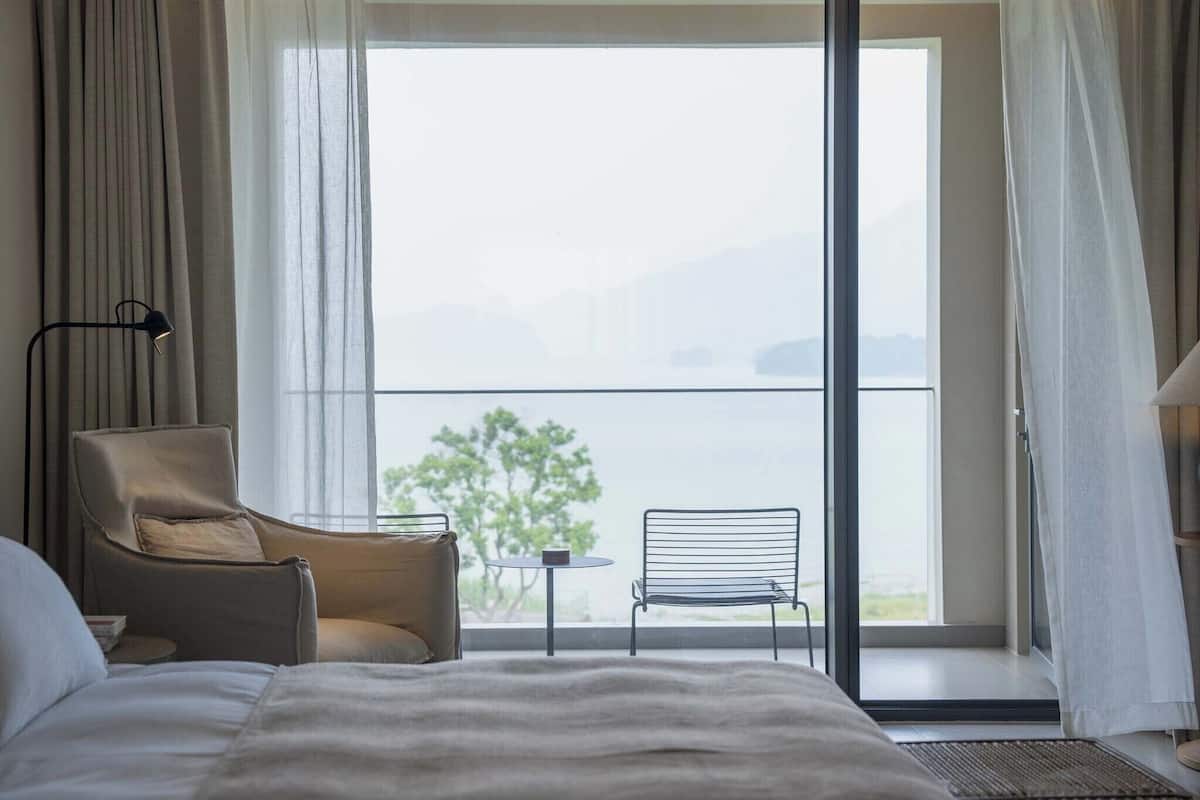 Ein Hotelzimmer mit Bett, Stuhl, kleinem Tisch und einem Balkon mit Blick ins Freie.