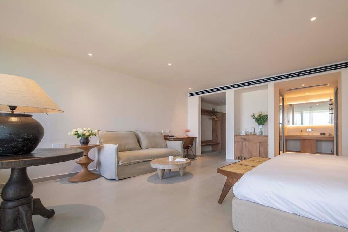Ein modernes Hotelzimmer mit einem großen Bett, einer Couch, einem kleinen Tisch, einer Lampe und einem Spiegel.