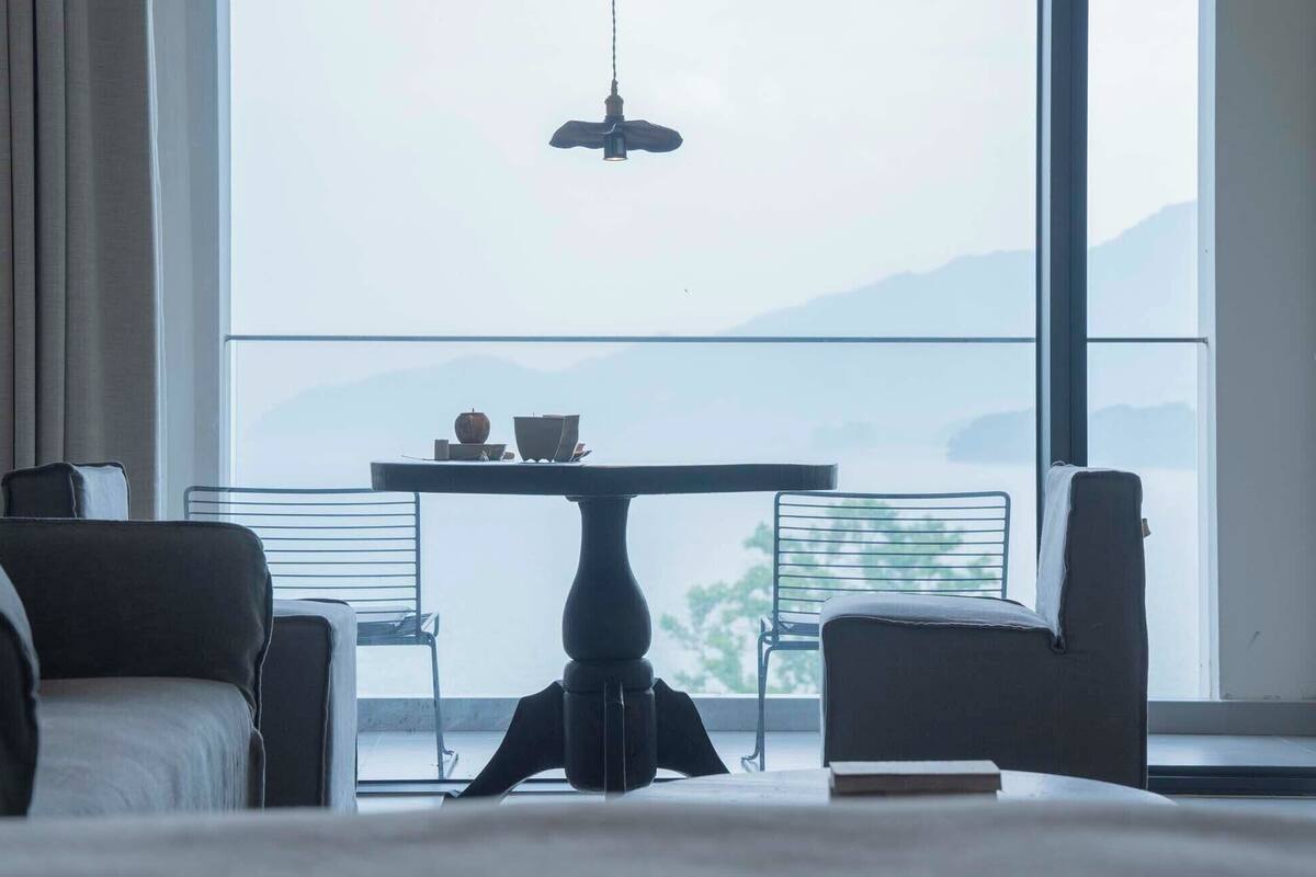 Ein modernes Hotelzimmer mit großem Fenster, einem Esstisch mit Stühlen und einer Hängelampe.