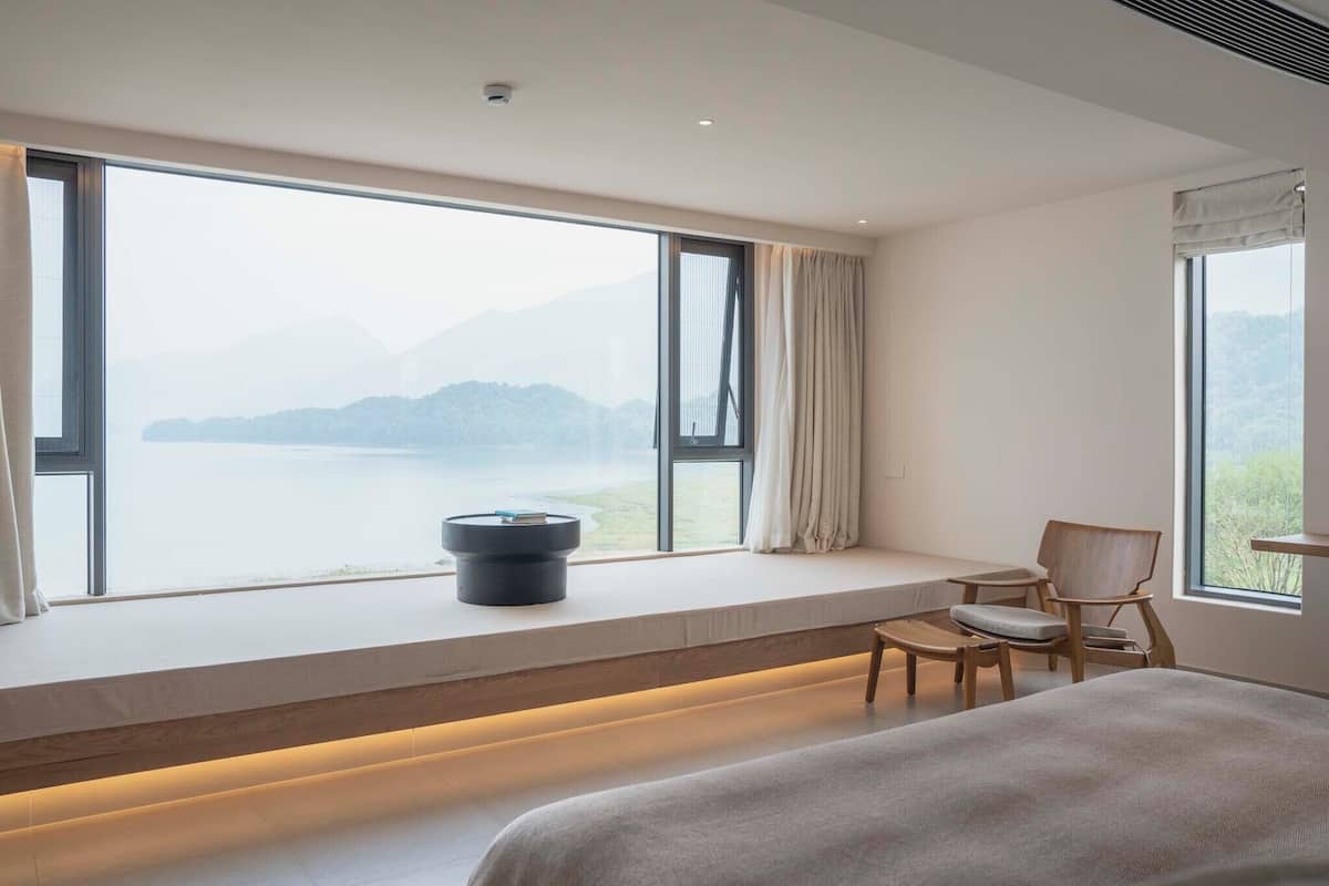 Ein Schlafzimmer mit großem Fenster, einem Bett, einem Nachttisch und einem Sessel.