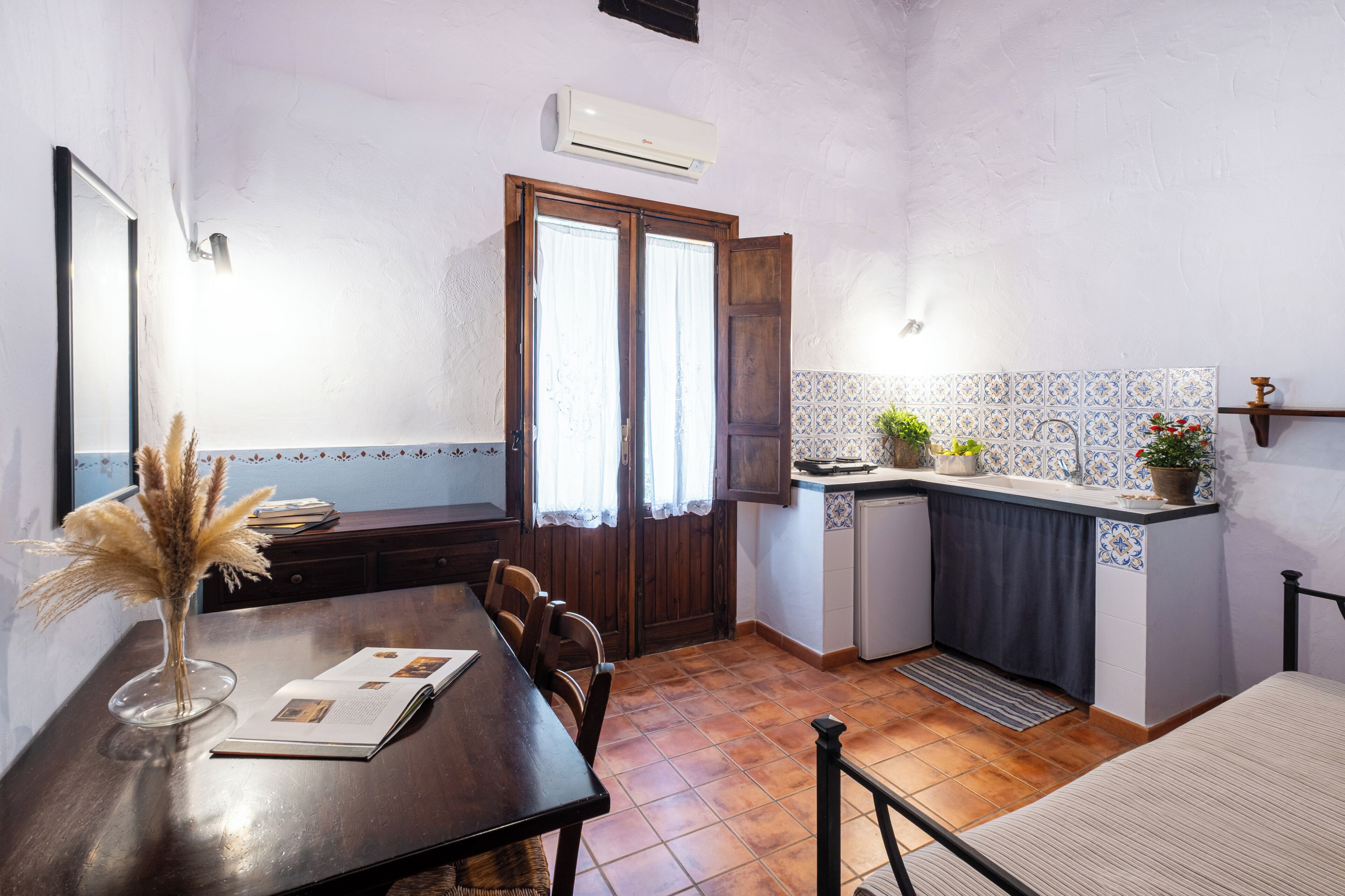 A compact kitchen with a dining area, featuring a wooden table, chairs, a small refrigerator, and a tiled backsplash.