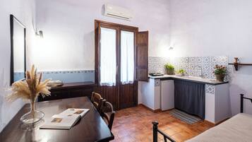 A compact kitchen with a dining area, featuring a wooden table, chairs, a small refrigerator, and a tiled backsplash.