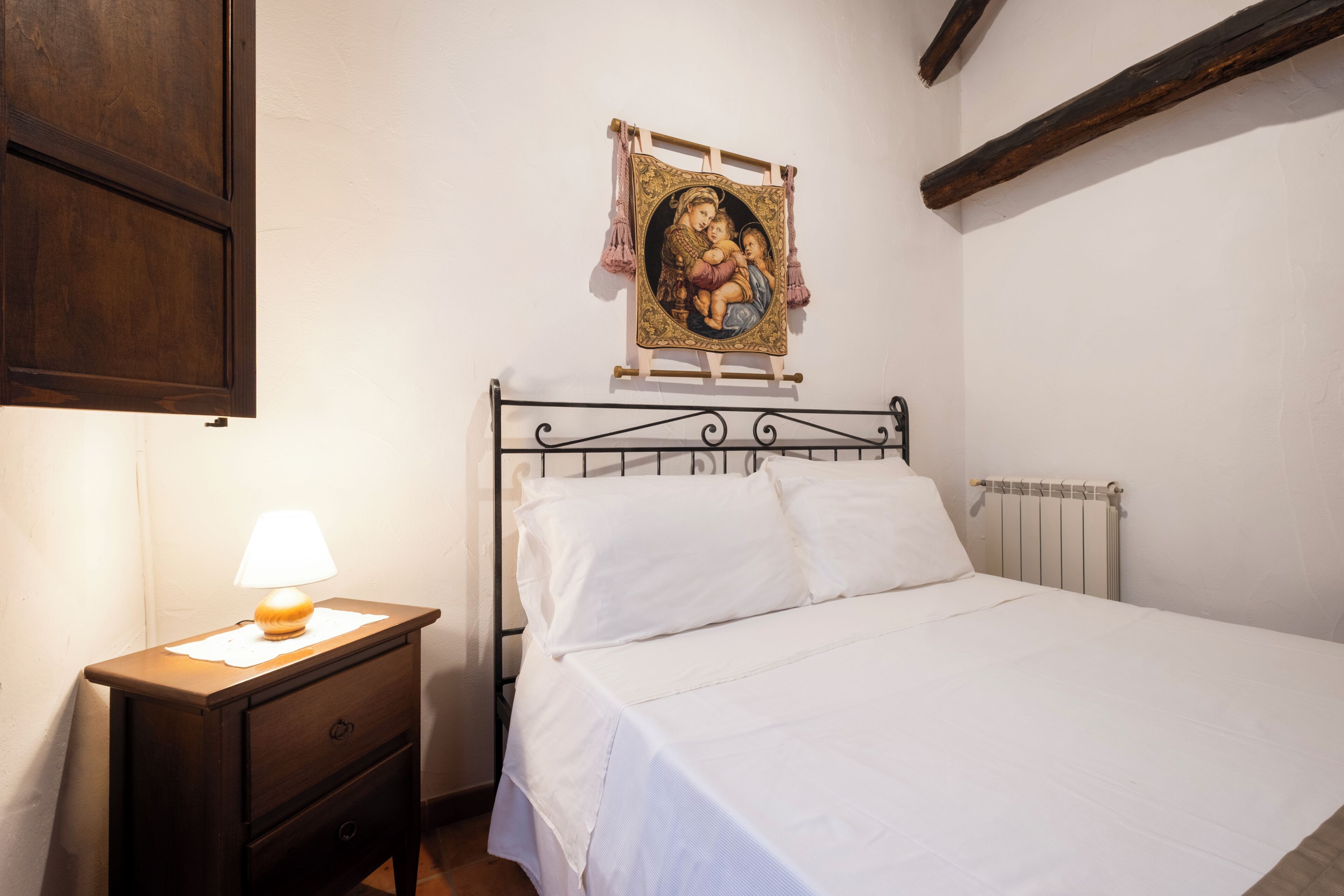 A bedroom with a bed, a nightstand with a lamp, and a wall-mounted picture.
