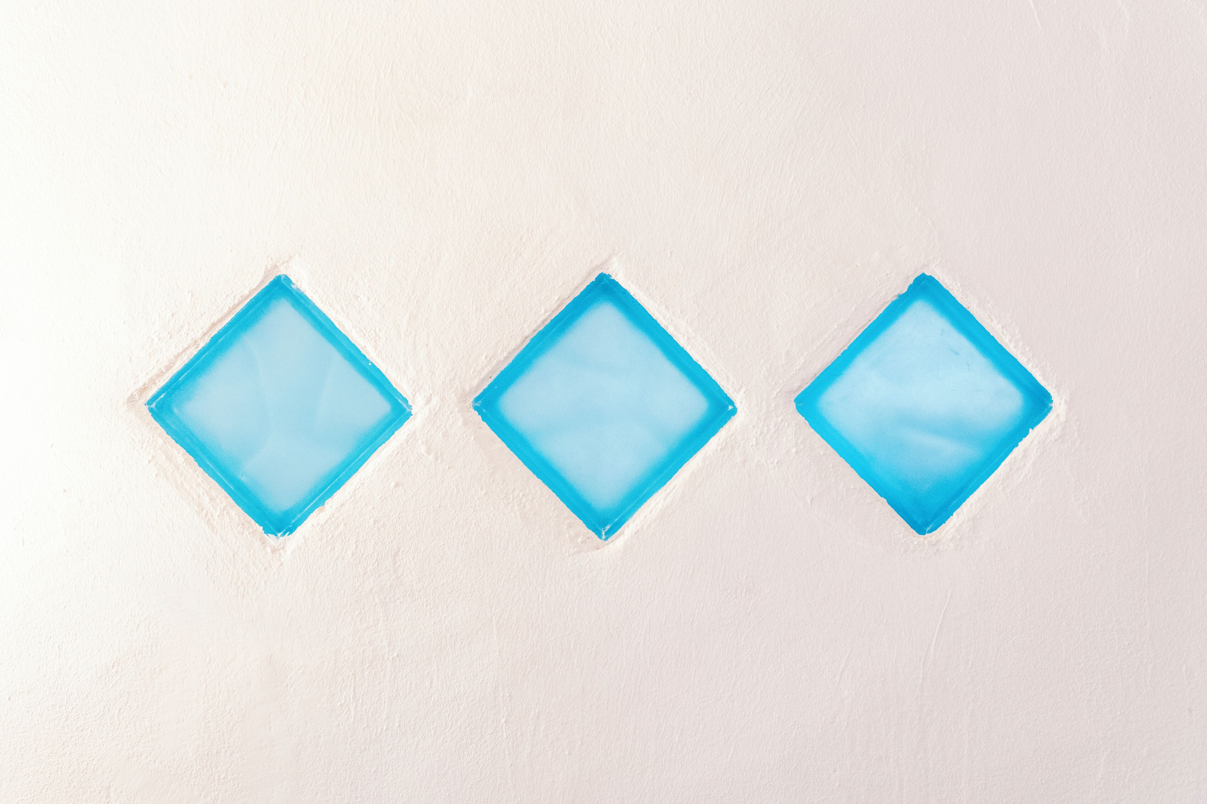 Tres objectes blaus en forma de diamant sobre una superfície blanca.