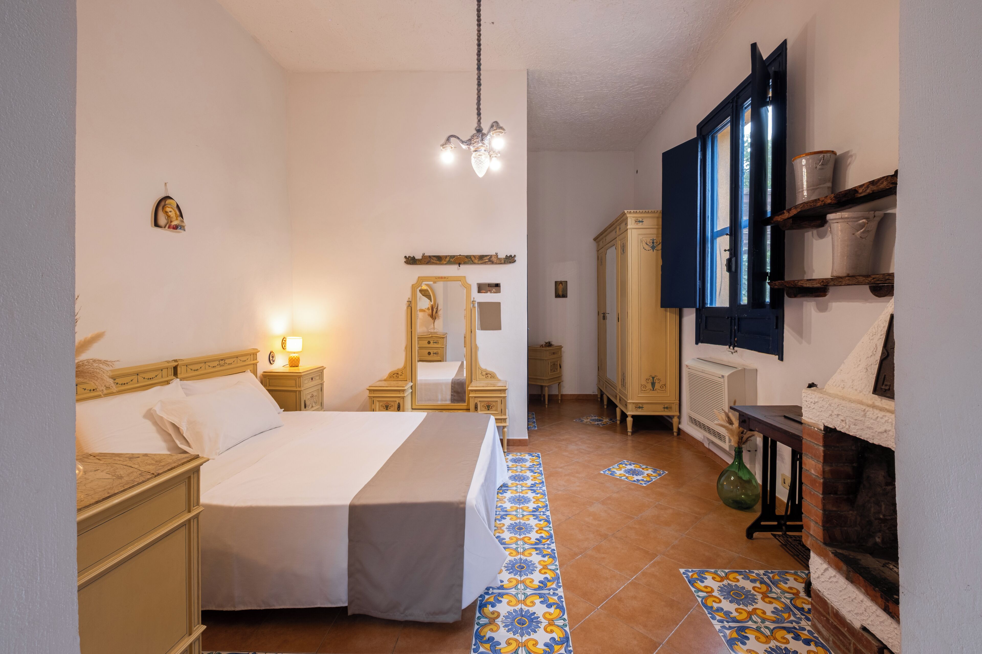 A hotel room with a bed, bedside tables, a mirror, a wardrobe, a radiator, and a fireplace.