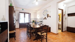 A dining area with a wooden table and chairs, a ceiling fan, and a kitchen visible through an open door. - Agriturismo Duca di Castelmonte (Trapani)
