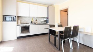 Una cucina moderna con mobili bianchi, un forno a microonde, un forno, un tavolo da pranzo con sedie e un pavimento piastrellato.