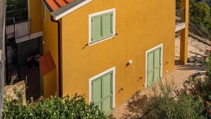 Un edificio giallo con tetto rosso, persiane verdi e vista sul mare.