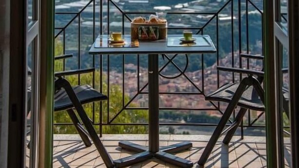 Un balcone con tavolo e sedie, vista su un fiume e montagne, e una ringhiera.