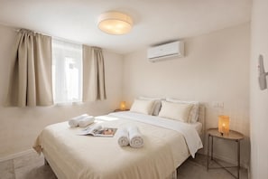 A hotel room with a bed, two bedside tables, an air conditioning unit, and a window with curtains.