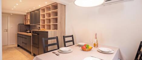 A modern kitchen with built-in appliances, a dining table set with plates and cutlery, and a fruit bowl.