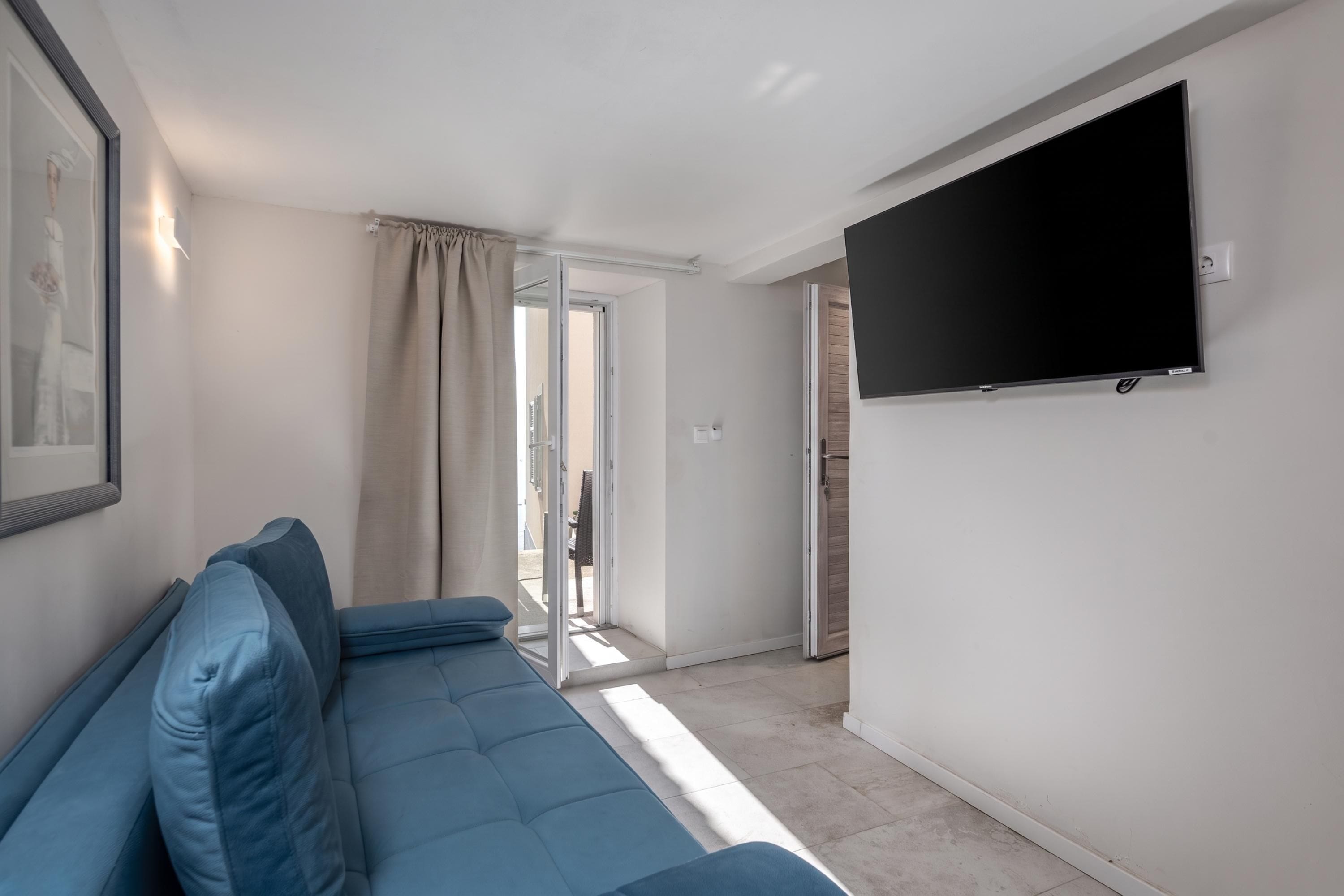 Un salon moderne avec un canapé bleu, un téléviseur à écran plat fixé au mur et une porte-fenêtre coulissante donnant sur un espace extérieur.