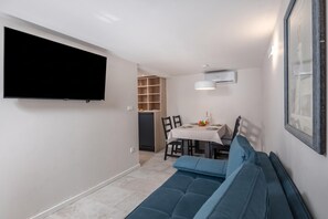 A compact living space with a flat-screen TV mounted on the wall, a dining area with a table and chairs, and a built-in bench with cushions.