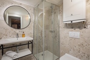 A modern bathroom with a glass-enclosed shower, a round mirror, and a white sink.