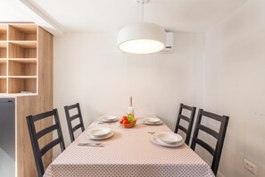A dining area with a table set for four, chairs, a basket of fruit, and a bottle of wine.