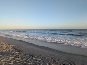 Ein Strand mit Wellen, blauem Himmel und sandigem Ufer.