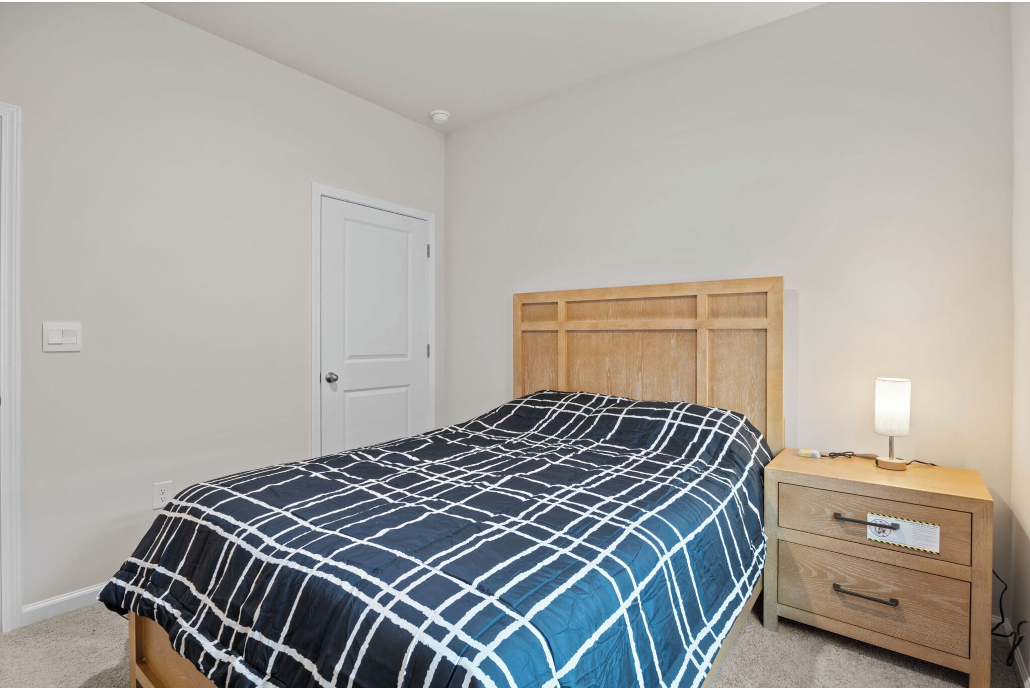 Ein Schlafzimmer mit einem Bett, einem Holzkopfende, einem Nachttisch mit Lampe und einer Tür.