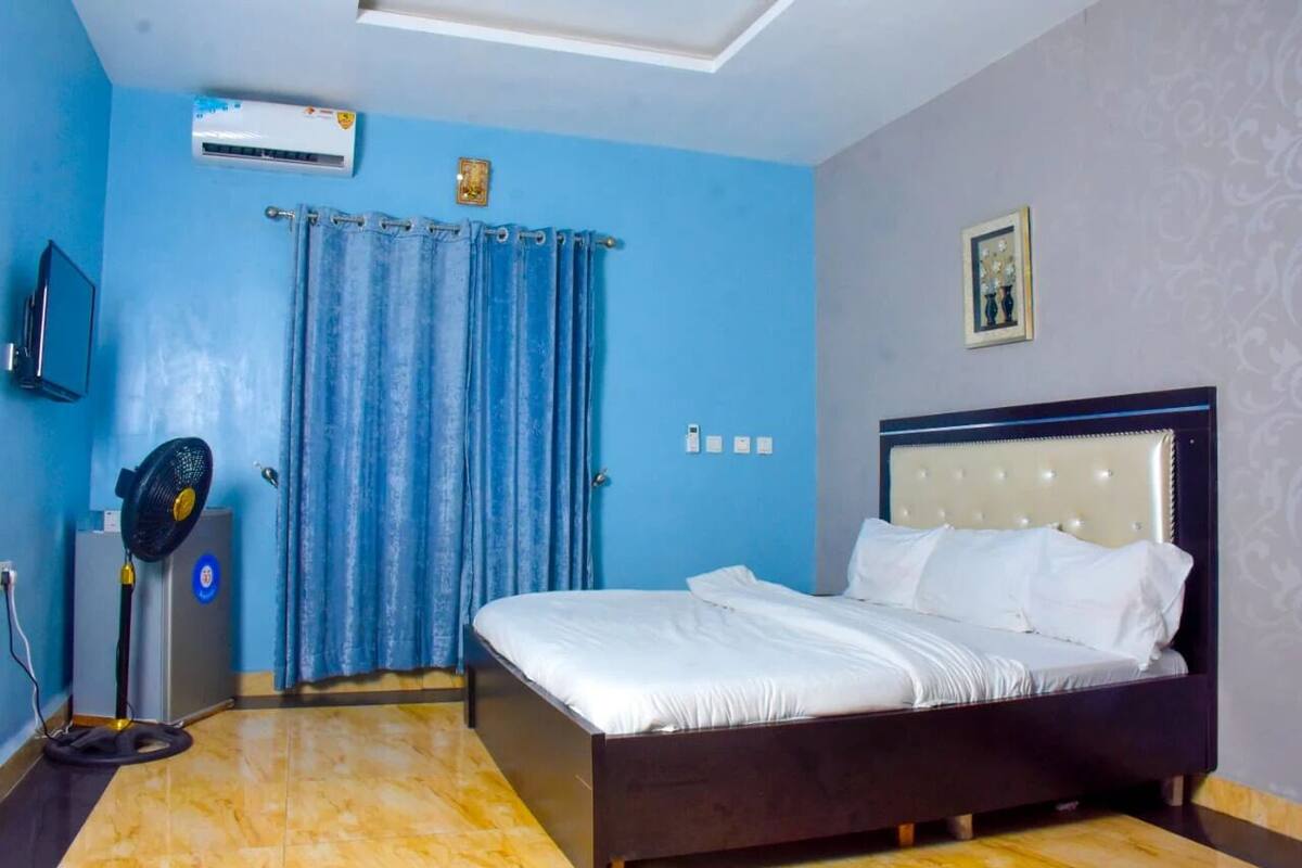 A bedroom with a bed, a ceiling fan, an air conditioner, a curtain, and a wall-mounted TV.
