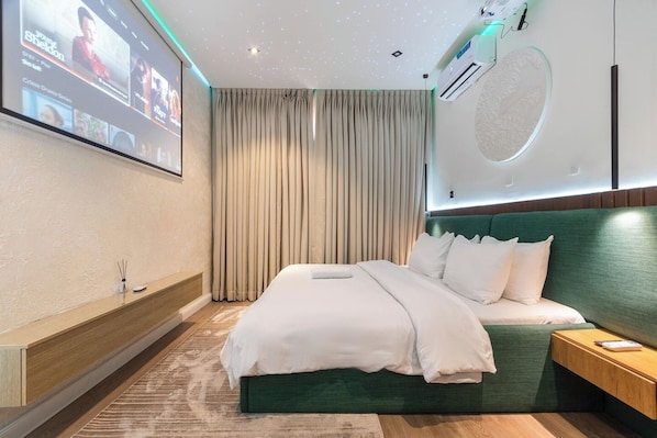 Habitación de hotel moderna con una cama grande, un televisor montado en la pared, un techo con diseño de estrellas y un ventanal con cortinas.