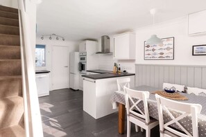 A compact kitchen with white cabinetry, a built-in oven, and a microwave. There's a dining area with a table and chairs, and a staircase leading to another room.