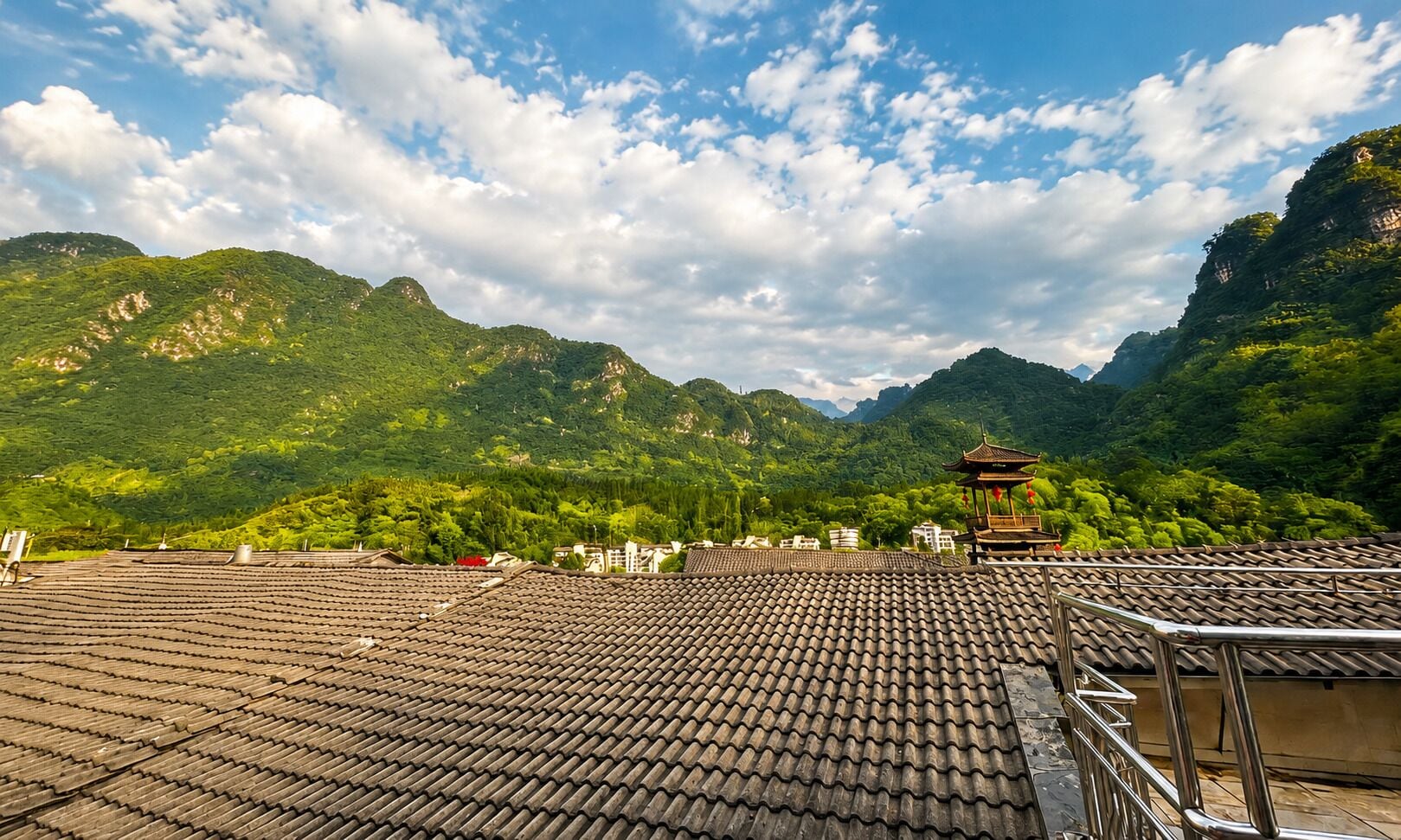 A traditional tiled roof, a pagoda, and lush green mountains in the background.