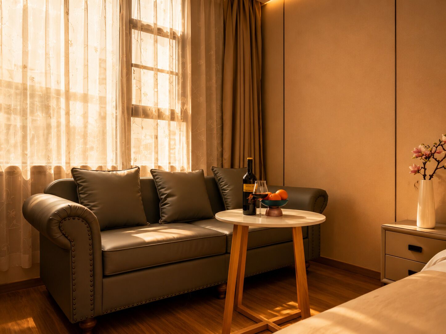 A cozy room with a leather sofa, a small wooden table with a bottle and glasses, and a vase with flowers.