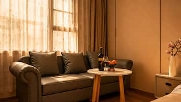 A cozy room with a leather sofa, a small wooden table with a bottle and glasses, and a vase with flowers.